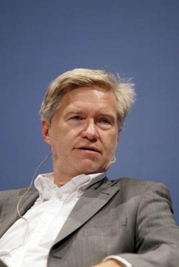Ein Mann mit blonden Haaren und grauem Anzug vor einem blauen Hintergrund.