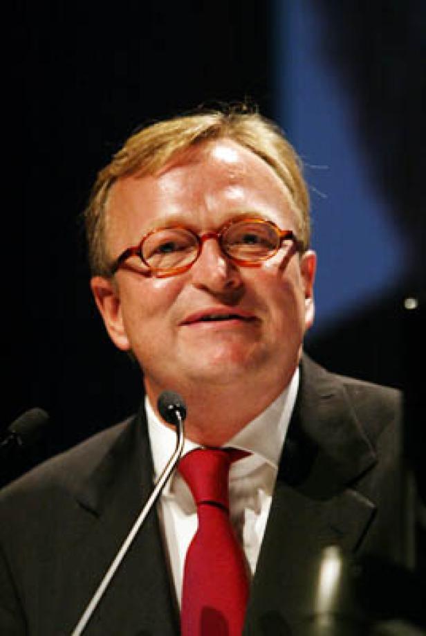 Ein Mann mit Brille und Anzug spricht vor einem Mikrofon.