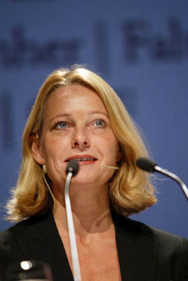 Eine blonde Frau spricht bei einer Konferenz in ein Mikrofon.