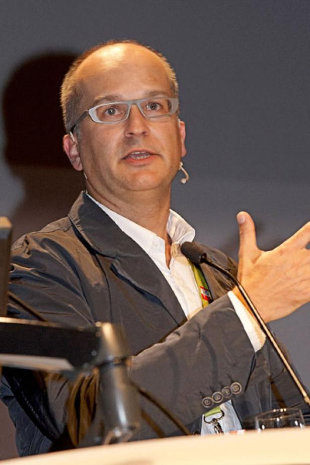 Ein Mann mit Brille gestikuliert an einem Rednerpult mit Mikrofon.