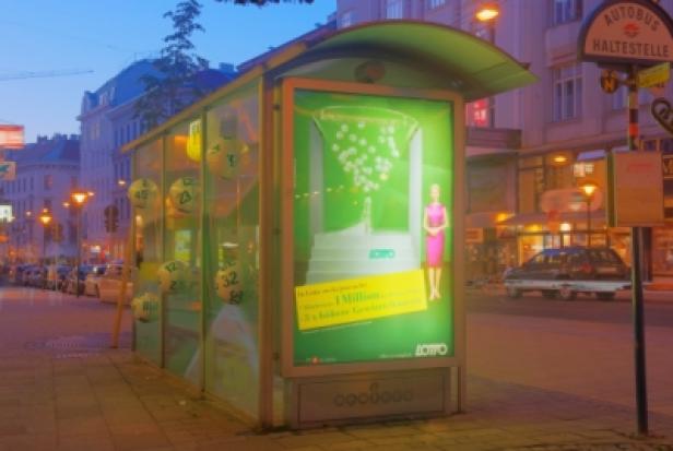 Eine Bushaltestelle mit einer Werbung für Lotto Österreich bei Dämmerung.