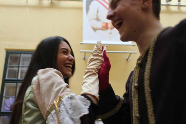 Zwei lachende Personen in historischen Kostümen halten Hände.