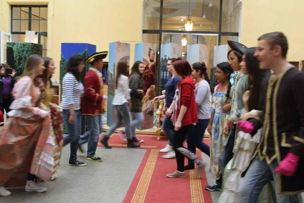 Eine Gruppe von Jugendlichen in Kostümen und Alltagskleidung geht über einen roten Teppich.