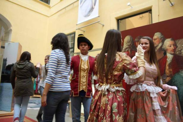 Besucher betrachten eine Ausstellung mit Personen in historischen Kostümen.