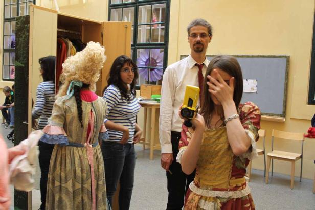 Eine junge Frau filmt mit einer gelben Kamera, während andere Personen im Hintergrund stehen.