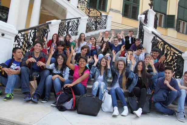 Eine Gruppe von Teenagern sitzt auf einer Treppe und winkt in die Kamera.