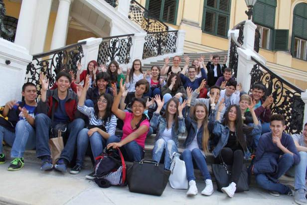 Eine Gruppe junger Leute sitzt auf einer Treppe und winkt in die Kamera.