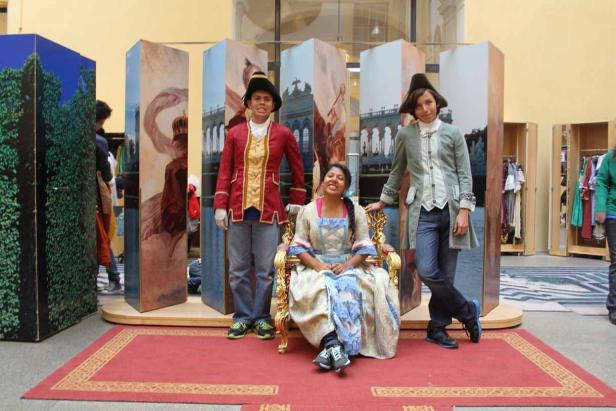 Drei Personen in historischen Kostümen posieren vor bemalten Kulissen.