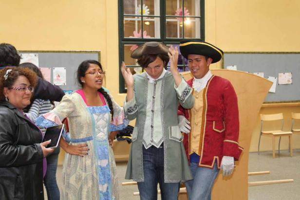 Drei Personen in Kostümen aus dem 18. Jahrhundert stehen in einem Raum.