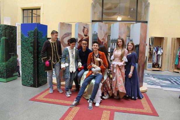 Eine Gruppe Jugendlicher in Kostümen posiert vor bemalten Kulissen.