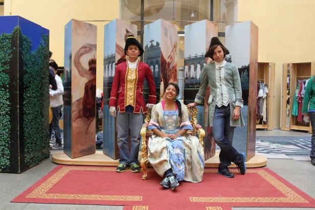 Drei Personen in Kostümen posieren vor bemalten Kulissen.