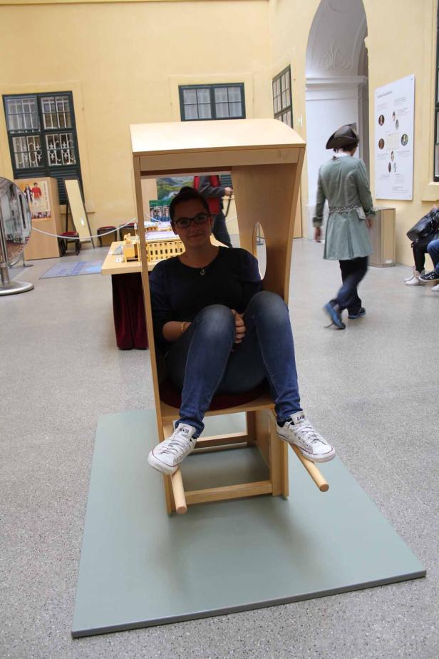 Eine Frau sitzt in einem hölzernen Sessel in einem Museum.