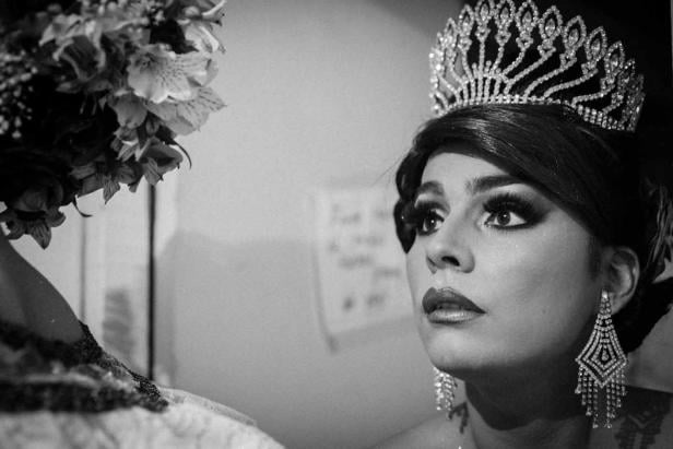 Eine Dragqueen mit Krone und auffälligen Ohrringen blickt nach oben.