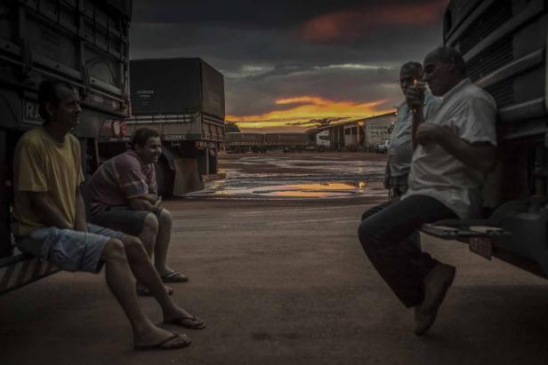 Vier Männer sitzen auf Lastwagen vor einem Lagerhaus bei Sonnenuntergang.