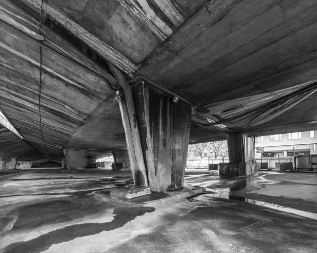 Eine Schwarzweißaufnahme der Betonstruktur einer Unterführung mit Wasserlachen auf dem Boden.