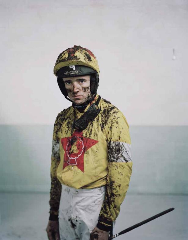 Ein Jockey, mit Schlamm bedeckt, steht nach einem Rennen da.