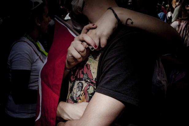 Eine Person umarmt eine andere, die ein T-Shirt mit Comic-Motiv und eine türkische Flagge trägt.