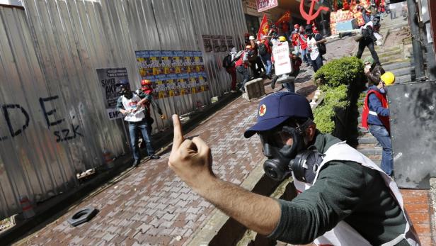Ein Demonstrant mit Gasmaske zeigt den Mittelfinger in Richtung einer Gruppe von Demonstranten.