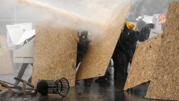 Demonstranten schützen sich mit Holzplatten vor einem Wasserwerfer.