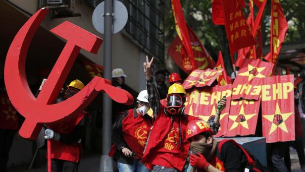 Demonstranten mit Schutzhelmen und Gasmasken tragen rote Fahnen und eine große Sichel und Hammer.