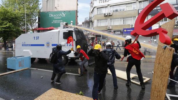 Ein Wasserwerfer der Polizei wird bei einer Demonstration gegen Protestierende eingesetzt, von denen einige Hammer und Sichel tragen.
