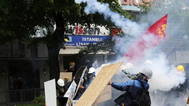 Demonstranten in Istanbul werfen mit Schutzschilden und einer TKP-Flagge in eine Rauchwolke.
