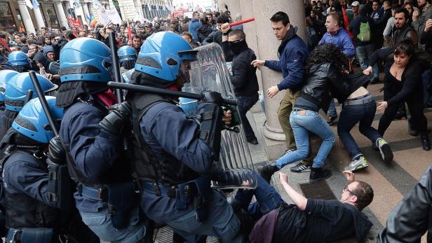 Polizisten in blauen Helmen stehen einer Menschenmenge bei einer Demonstration gegenüber.
