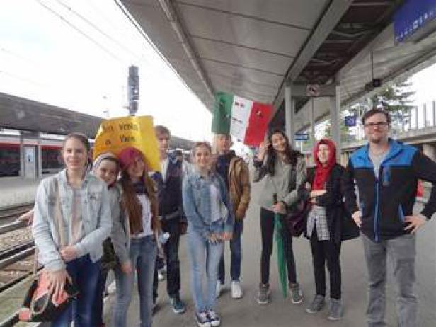 Eine Gruppe junger Leute steht mit einer Italienischen Flagge auf einem Bahnsteig.