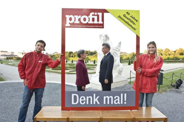 Zwei Personen halten einen „Profil“-Zeitschriftenrahmen mit dem Slogan „Denk mal!“ in einem Park.