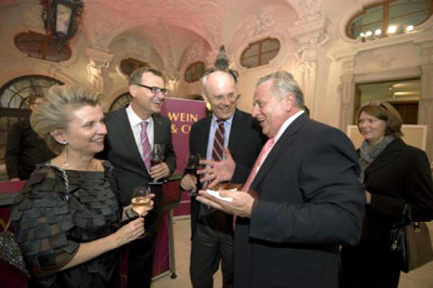 Eine Gruppe von Menschen unterhält sich bei einer Weinprobe in einem eleganten Saal.