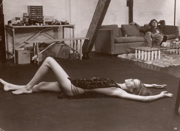 Eine Frau liegt auf dem Boden, während ein Mann auf einem Sofa im Hintergrund sitzt.