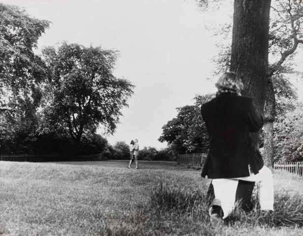 Ein Fotograf kniet auf einer Wiese, um ein Paar im Hintergrund zu fotografieren.