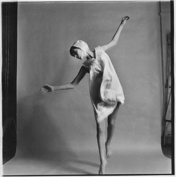 Eine junge Frau in einem Nachthemd und einer Haube balanciert auf einem Bein.