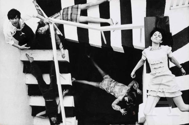 Eine Schwarz-Weiß-Fotografie von mehreren Personen in verschiedenen Posen auf einer Treppe und einem gestreiften Hintergrund.