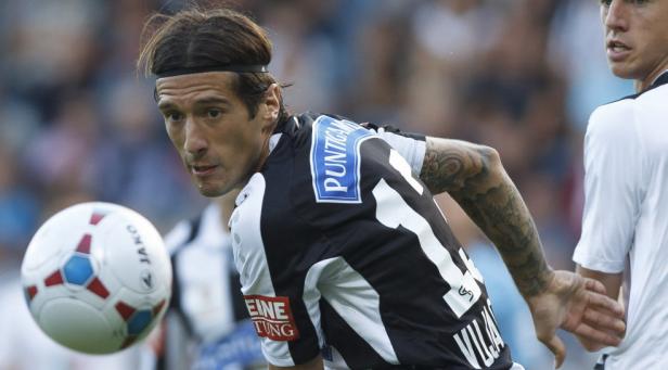 Ein Fußballspieler mit Tattoos am Arm blickt auf einen Fußball.