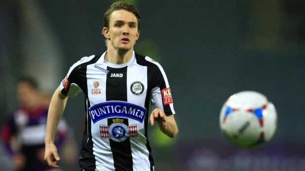 Ein Fußballspieler im schwarz-weißen Trikot des SK Sturm Graz mit einem Fußball.