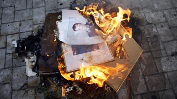 Gerahmte Fotos, darunter eines von einem Mann in Uniform, stehen in Flammen.