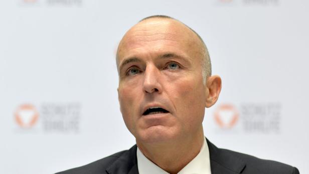 Ein Mann in einem dunklen Anzug spricht vor einem weißen Hintergrund.