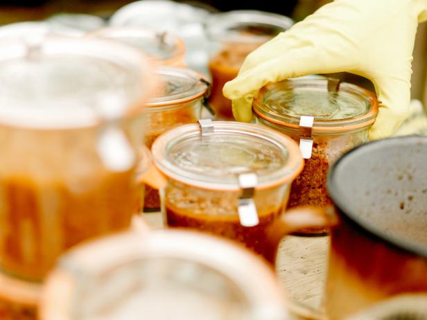Eine Hand mit gelbem Handschuh verschließt ein Einmachglas mit Chutney.
