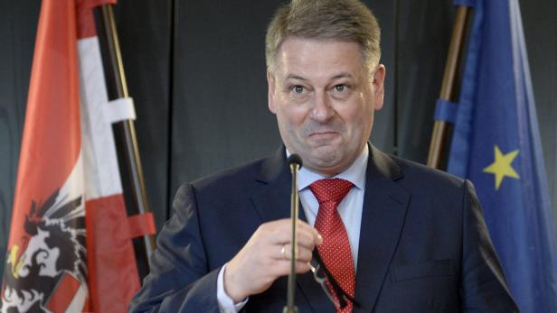 Ein Mann in Anzug und Krawatte steht vor der österreichischen und der EU-Flagge.