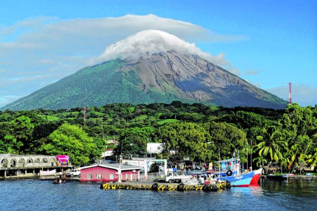 Ein Vulkan mit einer Wolke am Gipfel, gesehen von einem Hafen mit Booten.