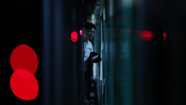 Ein Mann mit Brille steht nachts an einem Bahnsteig und blickt auf sein Handy.