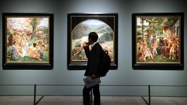 Ein Mann betrachtet drei großformatige Gemälde in einer Kunstgalerie.