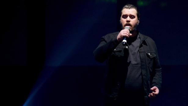 Ein Mann mit Bart singt in ein Mikrofon auf einer Bühne.