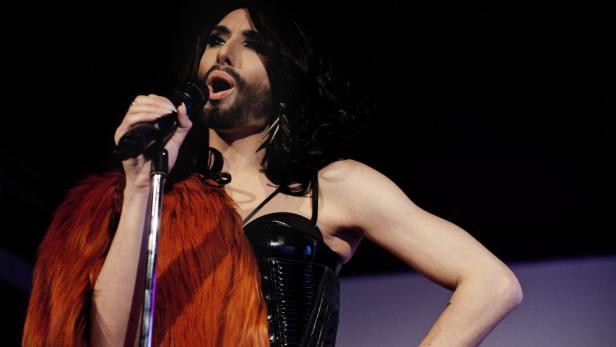 Conchita Wurst singt mit Mikrofon in der Hand auf einer Bühne.
