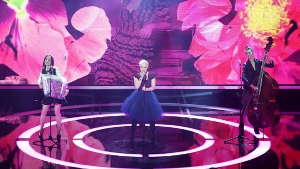 Drei Musikerinnen treten auf einer Bühne mit Blumenprojektionen auf.