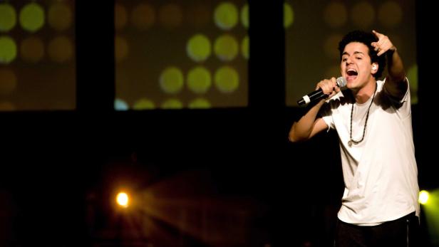 Ein junger Mann singt mit einem Mikrofon auf einer Bühne.