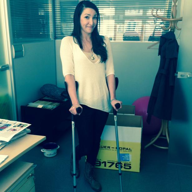 Laila Daneshmandi, Knie… Eine Frau mit Krücken steht in einem Büro.