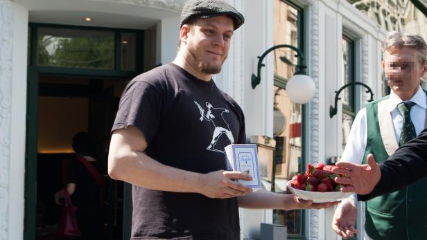 Ein Mann mit Schirmmütze hält Erdbeeren und eine Packung Würfelzucker.