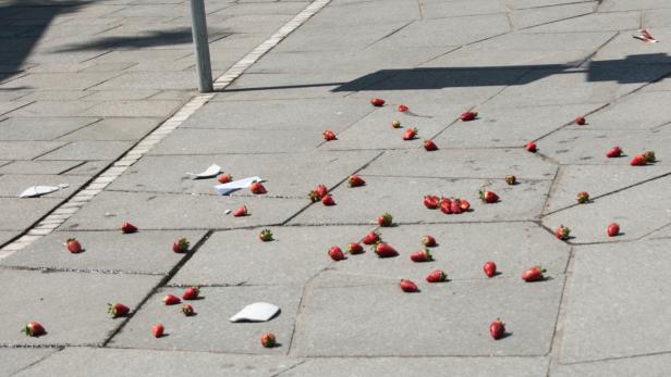 Auf einem Pflaster liegen verstreut Erdbeeren und Papierstücke.